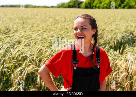 Glückliche Farmerin, die während der Wachstumssaison auf dem grünen Getreidefeld steht Stockfoto