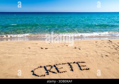 Erstellen Sie ein Wort aus Steinen am Sandstrand am klaren türkisfarbenen Meer in Mazida Ammos in der Nähe von Xerokambos im Osten Kretas, Griechenland. Sommerreise und min Stockfoto
