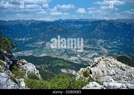 Hochauflösender Panoramablick von einem felsigen Berggipfel mit Blick auf ein weites Alpental mit kleinen Städten, bewirtschafteten Feldern, Wäldern, A Stockfoto