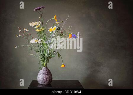 Blumenstrauß aus Wildblumen in einer kleinen Vase vor grauem Hintergrund. Stockfoto