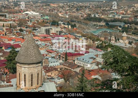 Tiflis, Georgien, 28.03.25: Hochwinkelansicht der vielfältigen Stadtarchitektur, Kirchenvorderseite, Fluss Mtkvari mit entfernter Friedensbrücke. Stockfoto
