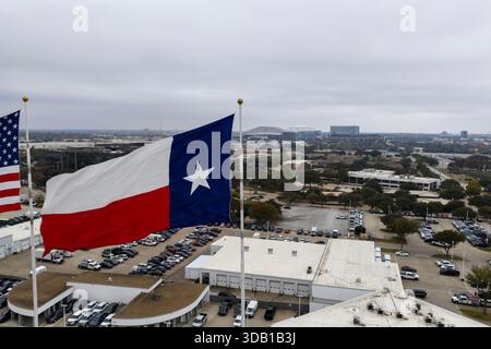 ARLINGTON, TX USA - 07. Dezember 2025: Aus der Vogelperspektive winken die amerikanischen und texanischen Bundesflaggen, die stolz im Wind winken, und ihre leuchtenden Farben klatschen in markanten, patriotischen Bewegungen über die Landschaft. Stockfoto