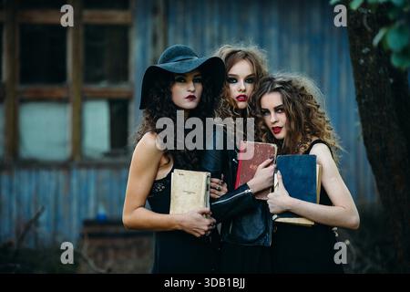 Drei alte Frauen als Hexen posieren vor einem verlassenen Gebäude mit Büchern in der Hand am Vorabend von Halloween || Model veröffentlicht Stockfoto