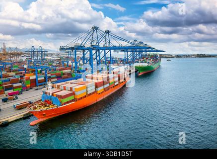 Ein großes Containerfrachtschiff wird von großen Kränen in einem gewerblichen Terminal-Dock be- und entladen Stockfoto