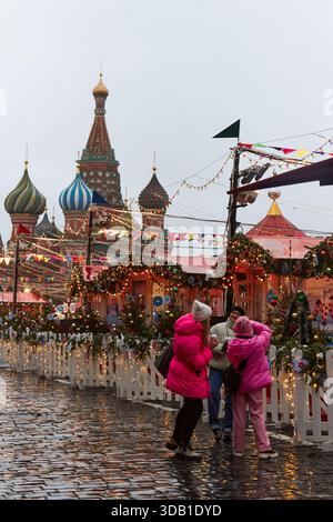 Moskau, Russische Föderation - 11. Dezember 2025: Auf dem Weihnachtsmarkt auf dem Roten Platz werden Besucher in rosa Jacken mit festlichen Dekorationen und St. Stockfoto