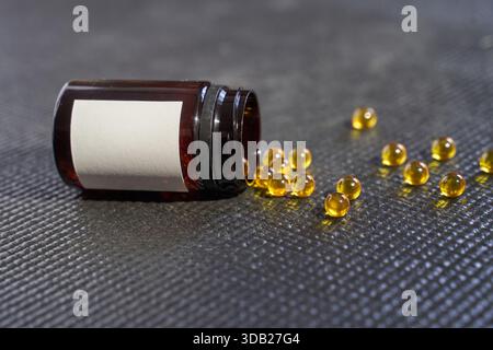 Verschüttete braune Kapseln aus brauner Flasche auf dunkel strukturierter Oberfläche. Stockfoto