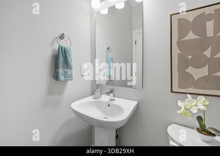 Badezimmer mit weißem Waschbecken und blauem Handtuch an der Wand. Das Waschbecken ist neben einem Spiegel und einem Bild an der Wand Stockfoto