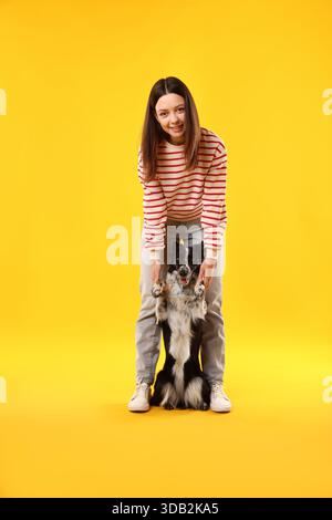 Frau mit ihrem süßen Border Collie Hund auf gelbem Hintergrund Stockfoto