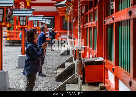 Ein Pilger betet mit gefalteten Händen vor der roten Schreinshalle von Kumano Hayatama Taisha in Shingū, Präfektur Wakayama. Der Schrein ist einer der drei großen Kumano-Schreine (Kumano Sanzan), neben Kumano Hongū Taisha und Kumano Nachi Taisha, und seit 2004 Teil des UNESCO-Welterbes "Heilige Stätten und Pilgerwege des Kii-Gebirges". Stockfoto