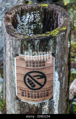 Ein Baumstumpf, der für den Pilzanbau auf dem Kumano Kodo in der Nähe von Shingū, Präfektur Wakayama, Japan, genutzt wird, trägt ein mehrsprachiges Schild mit der Aufschrift „Dies ist kein Mülleimer – bitte werfen Sie hier keinen Müll“. Kleine weiße Pilze wachsen aus dem ausgehöhlten Baumstamm. Stockfoto