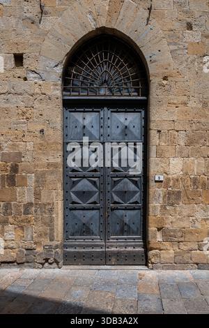 Mittelalterliches Holzportal des Palazzo dei priori in Volterra, schwere Stachelpaneele in rauem Sandsteinmauerwerk. Stockfoto