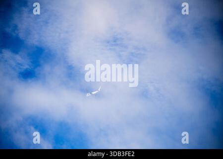 Ein Flugzeug bewegt sich durch helle Wolken in einem blauen Himmel, wobei weiches Licht über die Szene streut Stockfoto