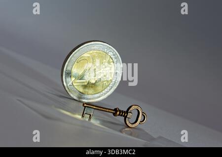 Zwei Euro-Münzen, die neben einem Vintage-Metallschlüssel auf reflektierender Oberfläche ausgeglichen sind. Starkes Symbol für Investitionen in die Sicherheit des Finanzzugangs und für wirtschaftliche Investitionen Stockfoto