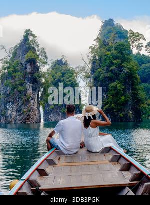 Erkunden Sie die faszinierende Schönheit des Cheow Lan Lake in Khao Sok, Thailand. Ein paar Männer und Frauen im Urlaub in Thailand, die bei Sonnenaufgang vor einem Longtail-Boot sitzen Stockfoto
