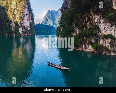 Erkunden Sie das ruhige Wasser des Cheow Lan Lake, umgeben von hoch aufragenden Kalksteinklippen und üppigem Grün. Ein Paar in einem Langboot in Khao Sok Thailand Stockfoto