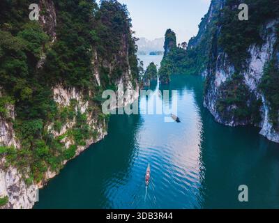 Erleben Sie die atemberaubende Schönheit des Cheow Lan Lake, umgeben von üppigen Klippen und ruhigen Gewässern. Kajakfahrer gleiten durch die atemberaubende Landschaft bei Sonnenaufgang, Khao Sok, Thailand Stockfoto