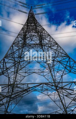 Elektrizitätspylon von unten mit Hochspannungsleitungen vor blauem Himmel mit Wolken Stockfoto
