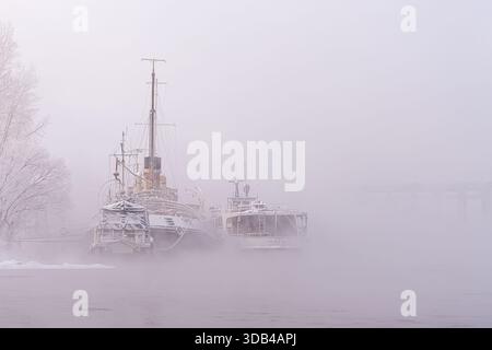 Atmosphärische Nebellandschaft mit nostalgischer Stimmung. Alte stillgelegte Schiffe, eine Jung-Straßenbahn und ein Schlepper oder ein Fluss-Eisbrecher permanent geparkt Stockfoto