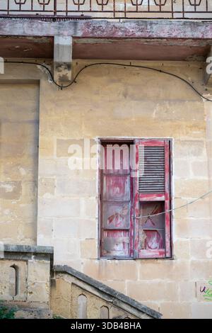 Ein altes Gebäude zeigt sein Alter. Der rote Fensterrahmen blättert ab und das Glas ist kaputt. Das Gebäude besteht aus Stein und die Treppe führt hinauf zum Stockfoto