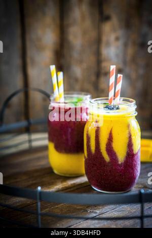 Bunte zwei Layer Mango und Berry Smoothies garniert mit Brombeeren Stockfoto