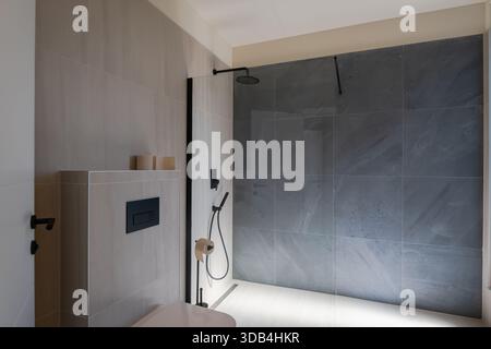Modernes, luxuriöses Badezimmer mit zwei Waschbecken, eleganten grauen Marmorfliesen, ebenerdiger Dusche und minimalistischer Toilette. Ein Spiegel reflektiert einen Blick Stockfoto