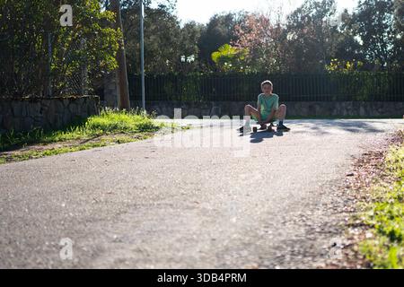 Ein Skater, der auf seinem Board in einer ruhigen Wohngegend ruht und die Nachmittagssonne genießt Stockfoto