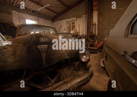 Staubiger Peugeot und Vintage Sedans in einem Scheunenfund - Autoreste in einer alten französischen Garage Stockfoto