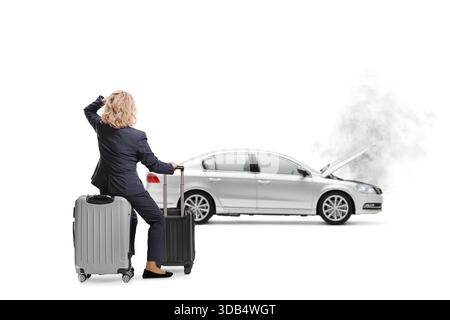 Rückansicht einer Frau, die auf einem Koffer sitzt und einen Pannenschaden auf weißem Hintergrund betrachtet Stockfoto