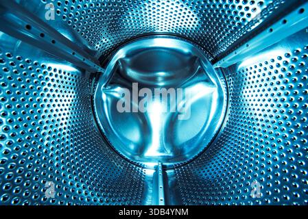 Nahaufnahme in einer Waschmaschinentrommel aus Edelstahl mit perforierter Metallstruktur und blauer Beleuchtung Stockfoto