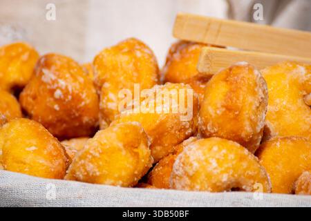 Nahaufnahme von gebratenem Teiggebäck mit weißem Zucker und Holzzange. Stockfoto