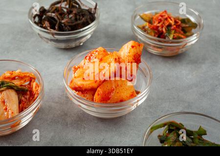 Blick auf eine kleine Schüssel koreanischer Radieschen-Kimchi, umgeben von verschiedenen Kimchi. Stockfoto