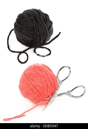 Zwei Garnknäuel, eine dunkelgrau/schwarz und eine Korallenrosa, werden neben einer verzierten Schere mit Vintage-Silberstickerei ausgestellt. Stockfoto