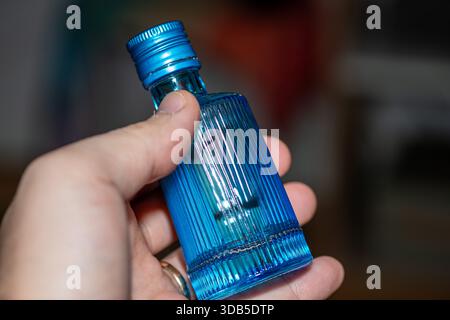 Ein detailliertes Nahfoto einer Hand mit einem kleinen blauen Glasfläschchen, das seine glatte Textur, Transparenz und klare Ästhetik des Produkts zeigt. Pe Stockfoto