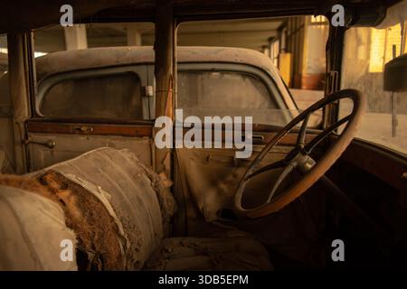 Verrostetes Oldtimer-Interieur mit abgerissener Polsterung und Holzlenkrad in einer verlassenen Garage Stockfoto