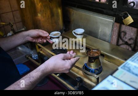 (251214) -- ISTANBUL, 14. Dezember 2025 (Xinhua) -- Can Ozmen, Besitzer des türkischen Cafés Mandabatmaz, macht türkischen Kaffee in seinem Café in Istanbul, T¨¹rkiye, 22. November 2025. Mandabatmaz, ein türkisches Café, befindet sich in einer kleinen Gasse neben der Istiklal Avenue in Istanbul. Der Besitzer, Can Ozmen, übernahm dieses kleine Café mit einer Geschichte von fast 60 Jahren von seinen Eltern. Um die Tradition fortzusetzen, besteht er immer noch darauf, Kaffee mit Kupfertöpfen zu brühen. Ozmen führte ein, dass türkischer Kaffee mit Kaffeesatz konsumiert werden sollte, was türkischen Kaffee einzigartig macht. Im Gegensatz zu anderen Kaffees, die es sind Stockfoto