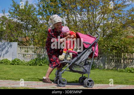 Die ältere Frau holt das Baby vom Kinderwagen ab Stockfoto