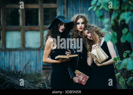 Drei alte Frauen als Hexen posieren vor einem verlassenen Gebäude mit Büchern in der Hand am Vorabend von Halloween || Model veröffentlicht Stockfoto