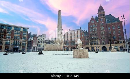 Verschneite Stadt Amsterdam am Damplatz in den Niederlanden im Winter bei Sonnenuntergang Stockfoto