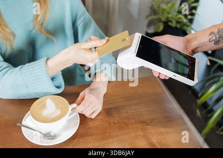 Der Kunde bezahlt für Kaffee mit NFC-Bankkarte am Handheld-POS-Terminal während der Kasse am Tisch in der kontaktlosen Bezahltechnologie des Cafés Stockfoto