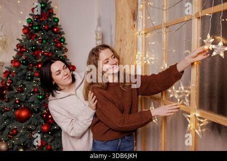Zwei Frauen teilen sich einen warmen Moment, während sie leuchtende Sternenlichter in einem gemütlich eingerichteten Haus hängen. Stockfoto