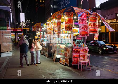 New York City, NY, USA - 10. Dezember 2025: Touristen kaufen und essen Fast Food an einem Imbissstand, der am Rande eines Bürgersteigs in Manhattan während des späten Nigs geparkt ist Stockfoto