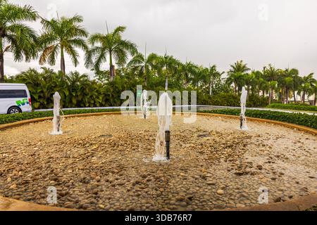 Wunderschöner Blick auf den runden Brunnen mit Wasserstrahlen umgeben von Palmen und tropischem Grün. Dominikanische Republik. Punta Cana. Stockfoto