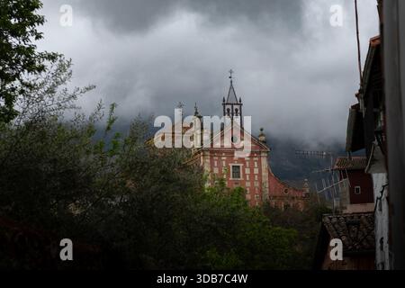 Historische Kirche, die sich über dem Dorf Hervás in Extremadura erhebt, mit dramatischen Sturmwolken und Bergnebel, die an Erbe, Spiritualität und r Stockfoto