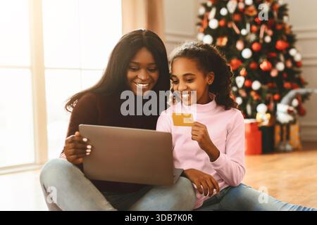 Mutter und Tochter kaufen sich in der Weihnachtszeit gemeinsam vor dem Weihnachtsbaum ein Stockfoto