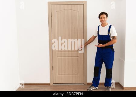 Ein professioneller Schlosser installiert ein neues Schloss an der Eingangstür, während er in blauer Uniform lächelt Stockfoto
