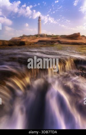 Dramatische Meereslandschaft mit mächtigen Meereswellen, die in den Vordergrund stürzen, mit dem historischen Trafalgar Lighthouse im Hintergrund, der sich im Süden befindet Stockfoto