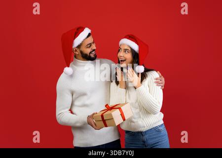 Überraschende Ehefrau mit Weihnachtsgeschenk von liebevollem Ehemann in festlicher Atmosphäre Stockfoto