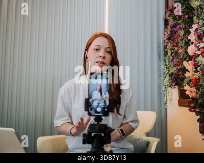 Frau spricht mit der Kamera, während sie auf einem Smartphone auf einem Stativ aufgenommen wird. Influencer-Inhalte, Online-Kommunikation und Creator Economy-Konzept. Stockfoto