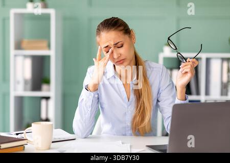 Müde Büroangestellte fühlt sich am Schreibtisch nach langen Stunden auf dem Laptop gestresst und erschöpft Stockfoto