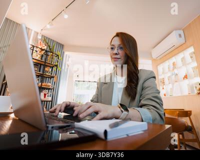Eine professionelle Frau mit Brille arbeitet an einem Laptop an einem Cafétisch. Konzept der Fernarbeit, Produktivität und Unternehmergeist. Stockfoto